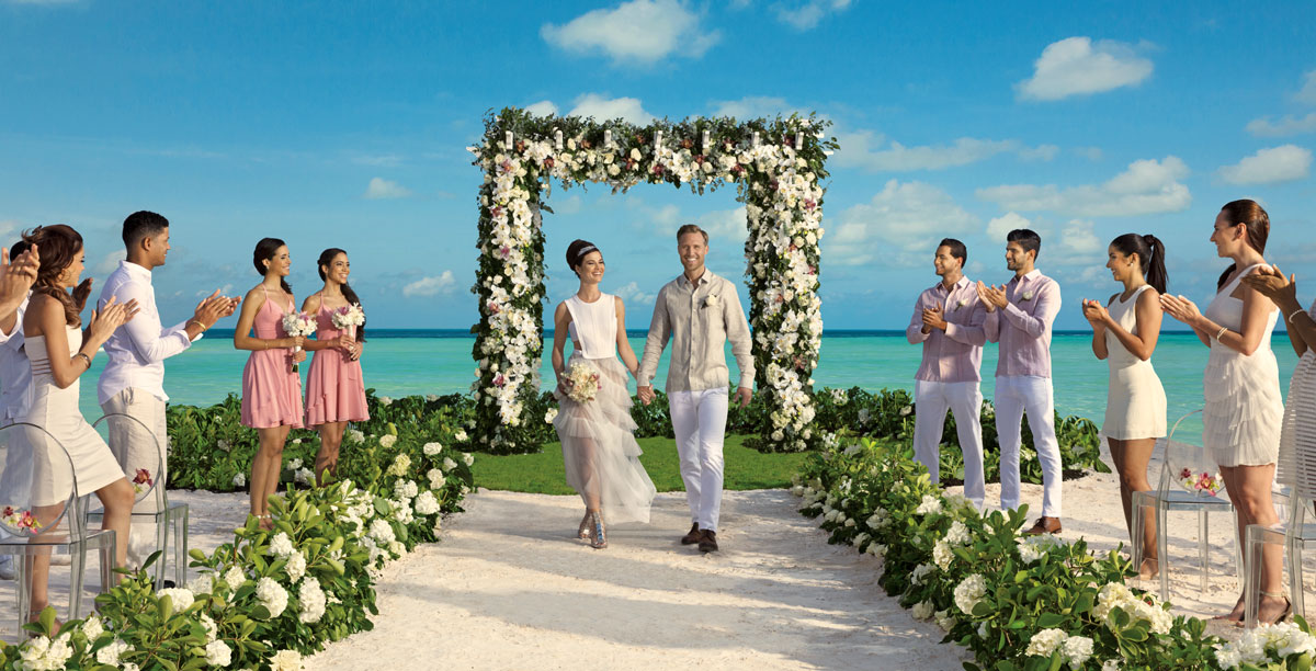 Newlyweds exiting beachfront wedding with applauding guests