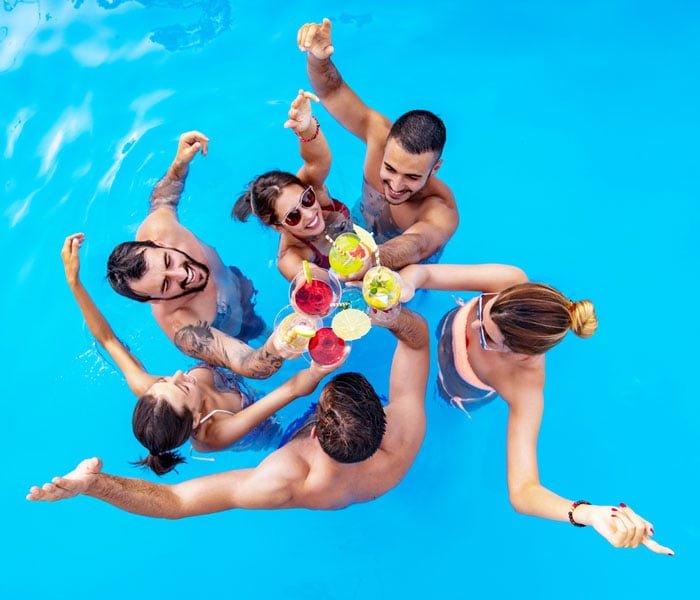 Group of friends having party in pool and drinking cocktails 