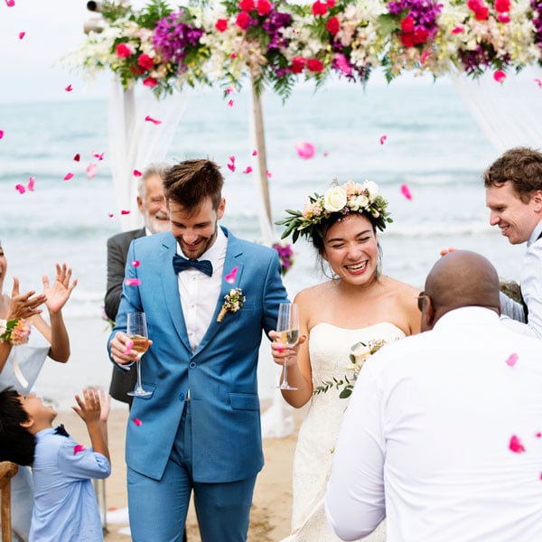 Couple on wedding day at beach with smiling guests in background